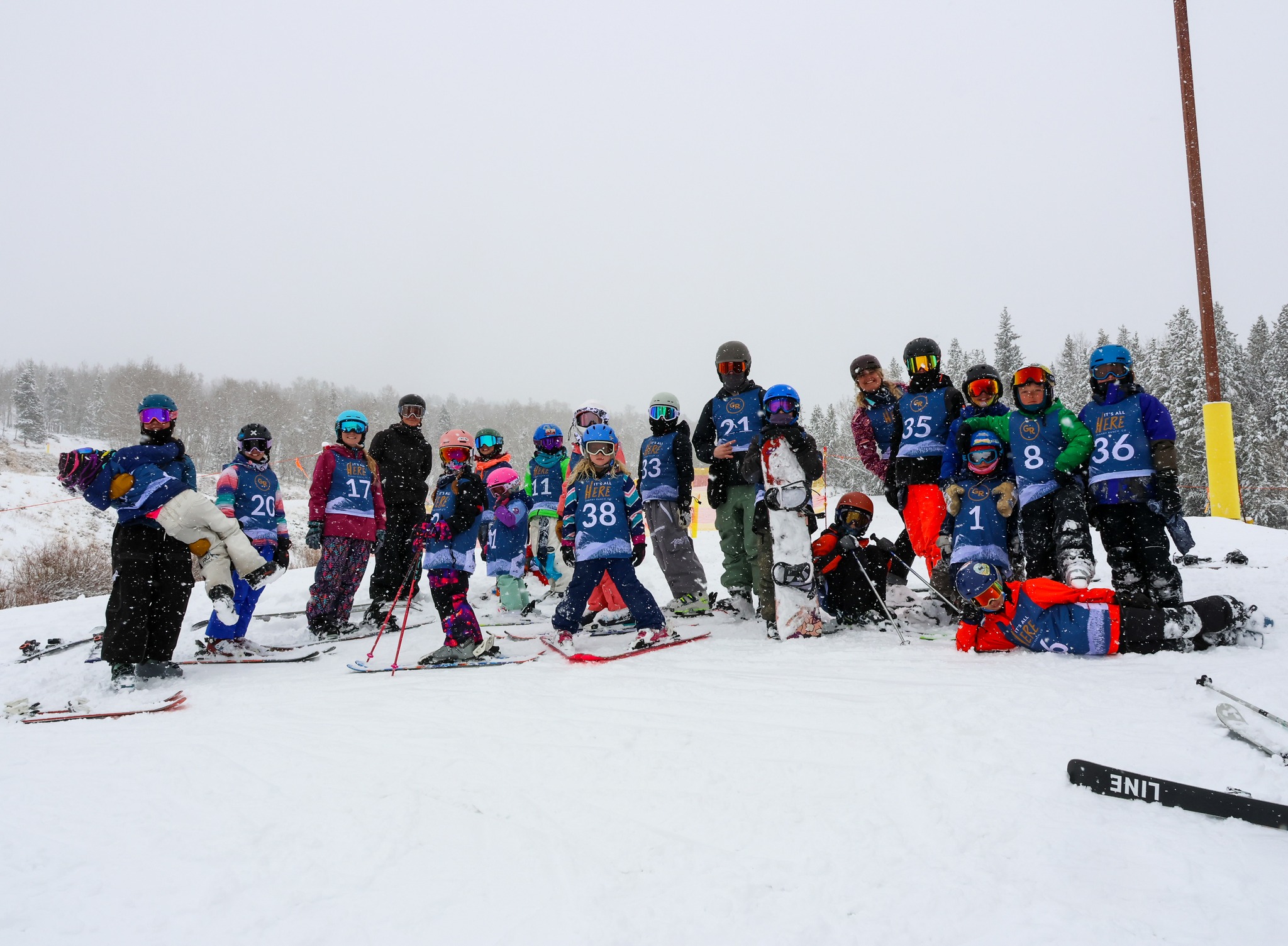 Group of young skiers and snowboarders in Granby Ranch race bibs posing on a snowy slope